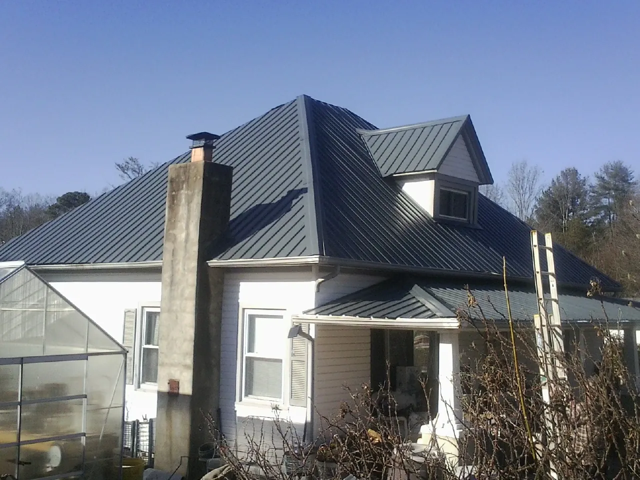 Dark blue standing seam metal roof on a white farmhouse with dormer — Slate & Tile Roof Repair by Roofing Brothers in Tracys Landing
