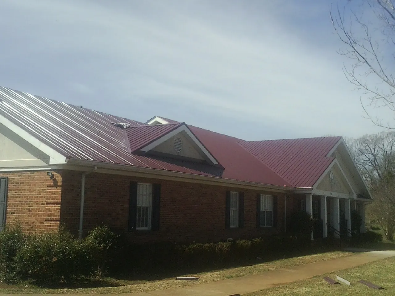 Red metal roof with gabled entries on a long brick building, from a Hail Damage Roof Repair job in Tracys Landing