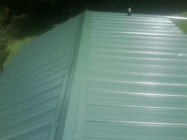 New green metal panels meeting at the ridge of a roof — Flat Roof Repair work by our crew in Tracys Landing