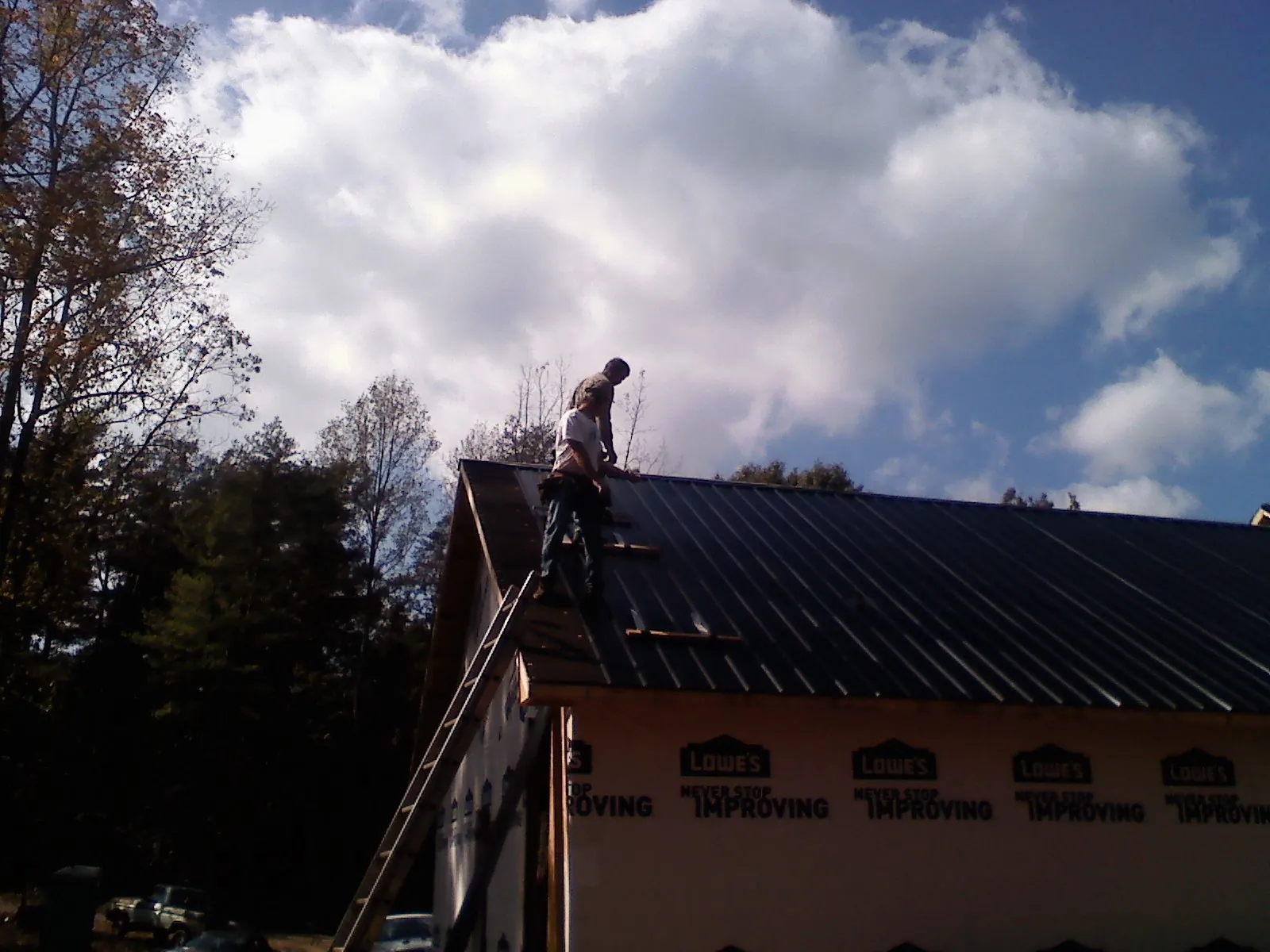 Roofer fastening dark metal panels high against a cloudy sky, from a Roof Inspection job in Tracys Landing