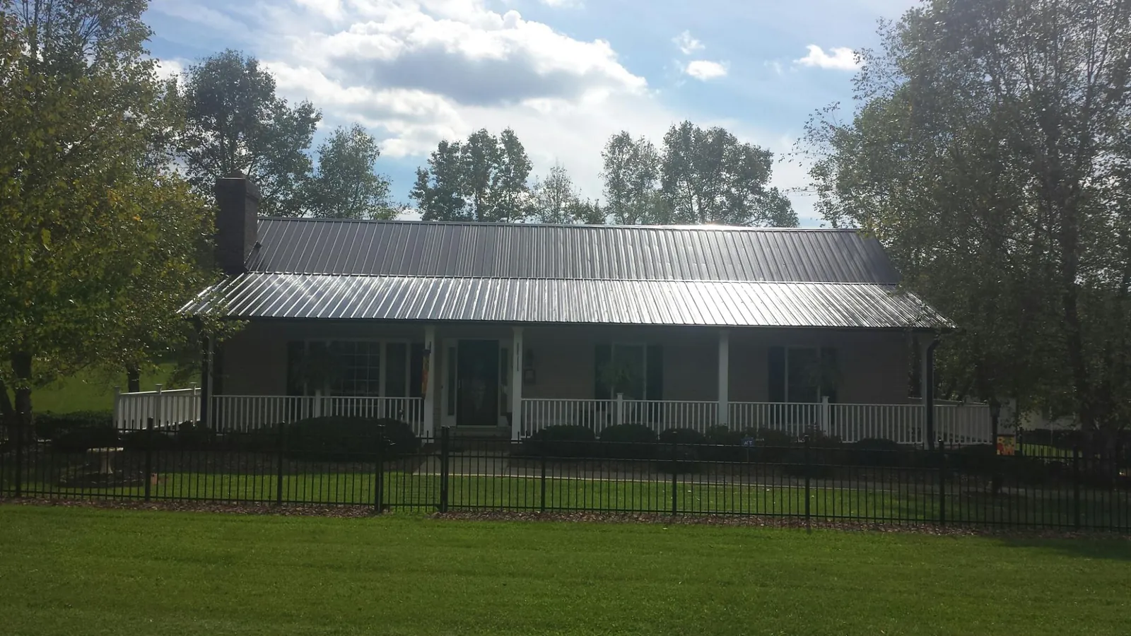 Gray metal roof on a brick ranch with a full width front porch — Gutter Guard Installation work by our crew in Tracys Landing