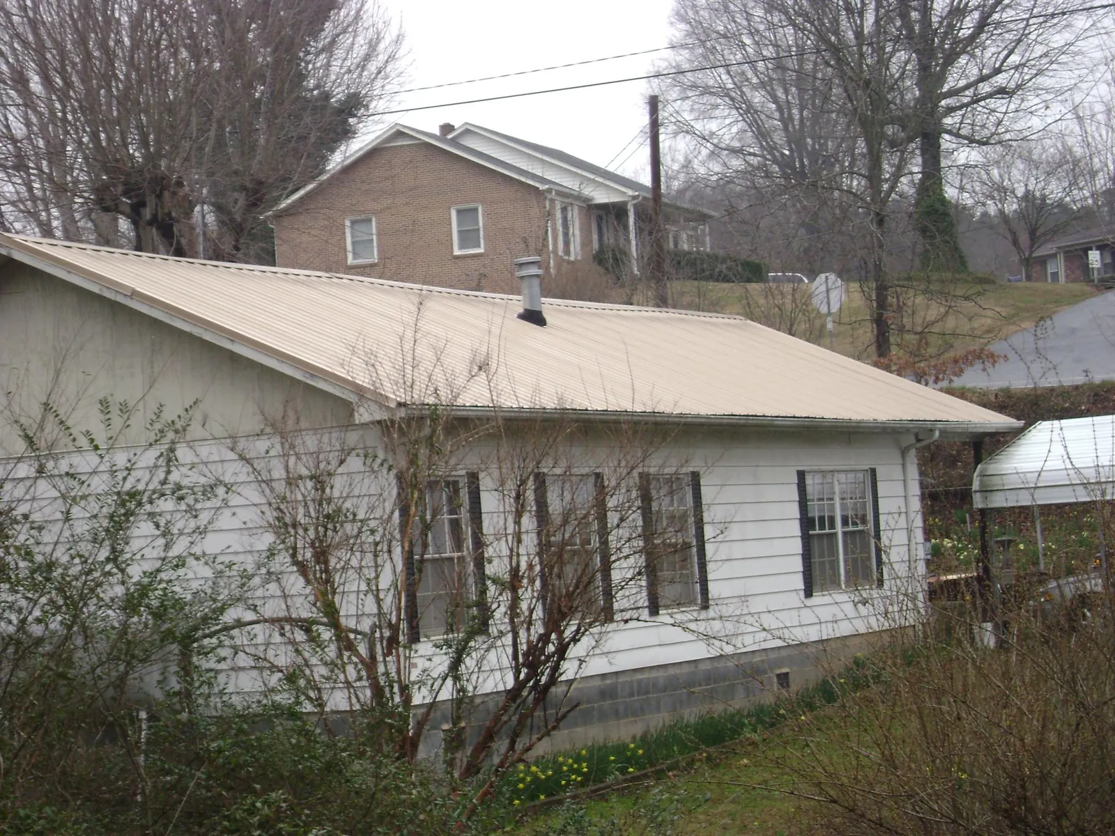 Tan metal roof on a white sided house set into a hillside — Commercial Roofing by Roofing Brothers in Tracys Landing
